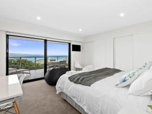 a white bedroom with a large bed and a balcony at Oceania 3 in Lorne