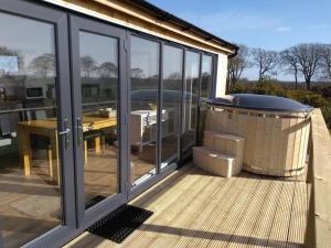 a deck with a hot tub and sliding glass doors at Cleeves Cabins Arran Luxury Lodge with hot tub in Dalry