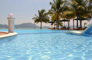 uma piscina num resort com palmeiras e um farol em The Ocean Residence Langkawi em Kuah