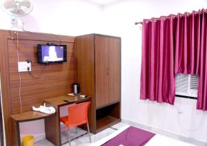 Habitación con escritorio, TV y cortina roja. en Hotel The Pride, en Kota