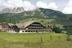 un grande edificio su un campo di fronte a una montagna di Hotel Rubino Deluxe a Campitello di Fassa