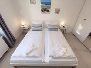 a room with a large white bed with two lamps at moderne Ferienwohnung mit eigener Terrasse - Haus Inselwind FeWo MEERhafen in Groß Zicker