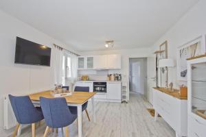 a white kitchen with a wooden table and blue chairs at moderne Ferienwohnung mit Balkon, Meerblick - Ferienresidenz Zwei BoddenFeWo 1-3 in Lietzow