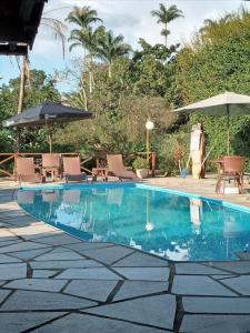 a swimming pool with chairs and umbrellas next to it at Pousada Vivenda Verde in Pirenópolis