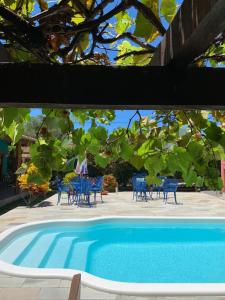 a blue swimming pool with chairs and a tree at Pousada Zimbauê in Itaúnas