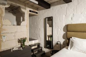 a bedroom with a white brick wall with a bed and a mirror at 19 ROOMS in Valletta