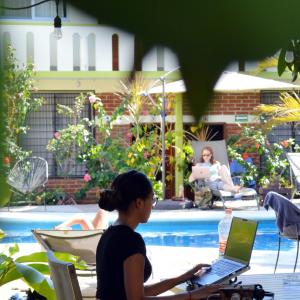 a woman sitting at a table with a laptop by a pool at Casa Losodeli & Coworking- Adults Only in Puerto Escondido