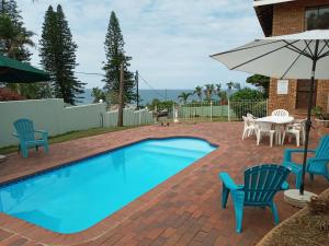 a swimming pool with chairs and a table and an umbrella at Rockview Guest House in Port Edward