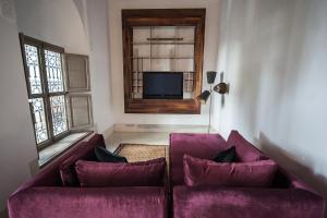 sala de estar con 2 sofás morados y TV en Riad Jaaneman, en Marrakech