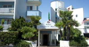 a building with a sign in front of palm trees at Hotel Cavalluccio Marino in Santa Marinella