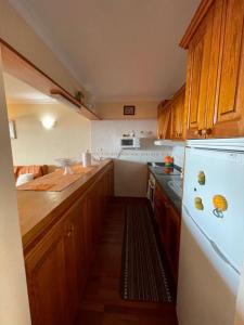 Una cocina con gabinetes de madera y un refrigerador blanco. en Apartamento Neptuno playa 17, en Puerto de Santiago