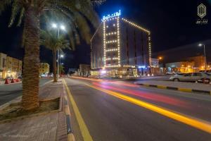 una strada di città di notte con un hotel e palme di أرائك توق a Sakakah