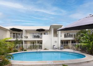 a swimming pool in front of a house with an umbrella at Noosa River Palms in Noosaville
