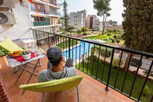 un uomo seduto su una sedia su un balcone che guarda una piscina di MONKÓ CACTUS a Torremolinos