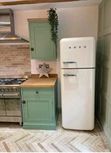 a kitchen with a white refrigerator and green cabinets at Ferry Lane Cottage in Kings Lynn