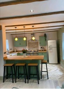 uma cozinha com armários verdes e uma ilha de cozinha com bancos em Ferry Lane Cottage em King's Lynn