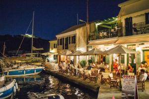 a group of people sitting at tables near a marina at night at Paxos StoneHouse in Gaios