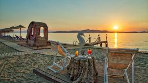 a table and chairs on a beach with a sunset at Venus Beach Hotel in Nea Stira