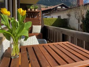 einen Holztisch mit einer Vase gelber Blumen auf dem Balkon in der Unterkunft Alpenflair Ferienwohnung 111 Nebelhorn in Oberstdorf