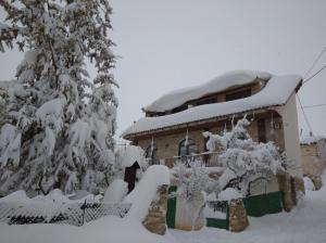 Casa Rural Chulilla في Villarroya de los Pinares: منزل مغطى بالثلج مع الأشجار أمامه