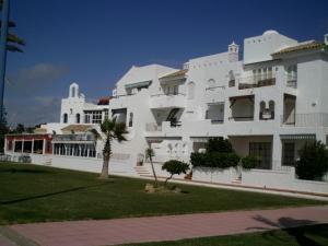 duży biały budynek z palmą przed nim w obiekcie Primera linea de playa "Barrosamar" w mieście Chiclana de la Frontera