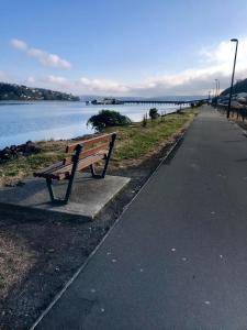 a bench sitting on the side of a path next to a lake at Harbour Side Views in Dunedin