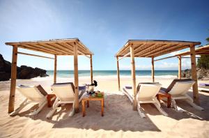 RIMBA by AYANA Bali في جيمباران: مجموعة من الكراسي وطاولة على الشاطئ