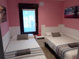 2 camas en una habitación con paredes rosas y ventana en Playa Laga, en Ibarrangelu
