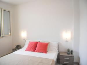 a bedroom with a white bed with two red pillows at Appartamenti Le vie di Omero in Torre dell'Orso