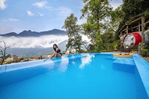 a woman sitting on the edge of a swimming pool with mountains in the background at Tubotel Sapa in Sa Pa