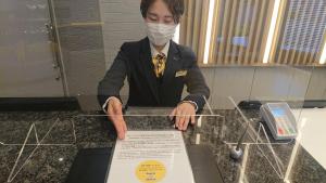 une personne portant un masque portant une pancarte sur un comptoir dans l'établissement Smile Hotel Aomori, à Aomori