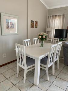 una mesa de comedor blanca con sillas y un jarrón de flores en Herolds Bay Accommodation - Smalstaan Upstairs, en Herolds Bay