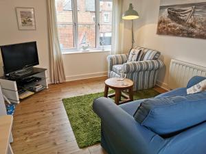 a living room with a blue couch and a tv at AnchorageWells Harbour Apartment in Wells next the Sea