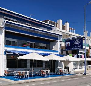 a restaurant with tables and umbrellas in front of a building at ''O Veleiro'' Rest. Resid. in Torreira