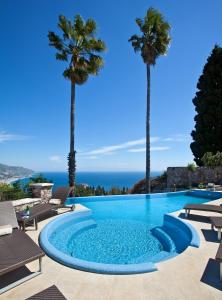una piscina con palme e l'oceano sullo sfondo di The Ashbee Hotel a Taormina