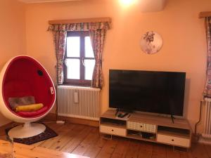 ein Wohnzimmer mit einem TV und einem großen roten Stuhl in der Unterkunft Weichselboden, Alte Schule in Weichselboden