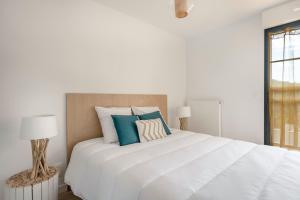 een witte slaapkamer met een groot wit bed met blauwe kussens bij Un sejour en appartement face a la mer a Pleneuf Val Andre in Pléneuf-Val-André