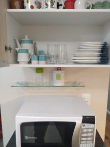 un four micro-ondes dans une cuisine avec des assiettes et de la vaisselle sur les étagères dans l'établissement Apartamento Tranquilo Próximo ao Aeroporto. Sem taxa de limpeza, à São José dos Pinhais