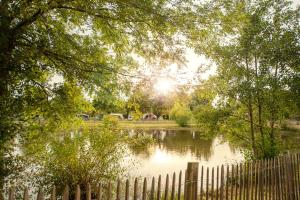 a fence in front of a pond with the sun shining at Camping RCN La Ferme du Latois in Coëx +22 photos