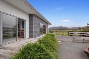 ein Haus mit einer Terrasse mit einer Bank und Gras in der Unterkunft A Reel Retreat - Waihi Beach Holiday Home in Waihi Beach