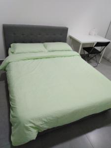 a bed with a green comforter and a table at Mayzi Holiday Home @ Cyberjaya in Cyberjaya