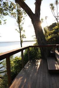 een houten terras met een boom en een bank bij Neptune Coastal Haven in Auckland