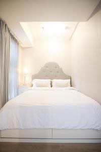 een witte slaapkamer met een groot bed met witte lakens bij CLASSICA by Kozystay - Kota Kasablanka in Jakarta