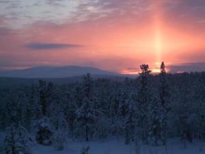 um pôr-do-sol sobre uma floresta coberta de neve com árvores em Holiday Home Kuukkelitupa by Interhome em Vuontisjärvi