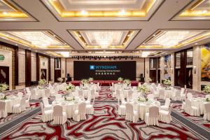 un salón de banquetes con mesas y sillas blancas y una pantalla en Wyndham Xinyang Downtown, en Xinyang