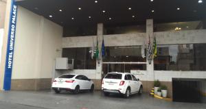 twee witte auto's geparkeerd voor een gebouw bij Grande Hotel Universo Palace in Uberlândia