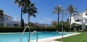una piscina frente a un edificio con palmeras en Marbella Holiday & Golf Garden Apartment, en Marbella