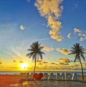 a bench on a beach with a palm tree and the words karma at Pousada Portal do Cabo in João Pessoa