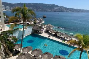 einen Luftblick auf einen Resortpool mit Sonnenschirmen und das Meer in der Unterkunft Suite frente al mar en el corazón de Acapulco in Acapulco
