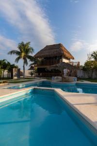 a swimming pool with a thatched building in the background at HOTEL & BEACH CLUB OJO DE AGUA in Puerto Morelos